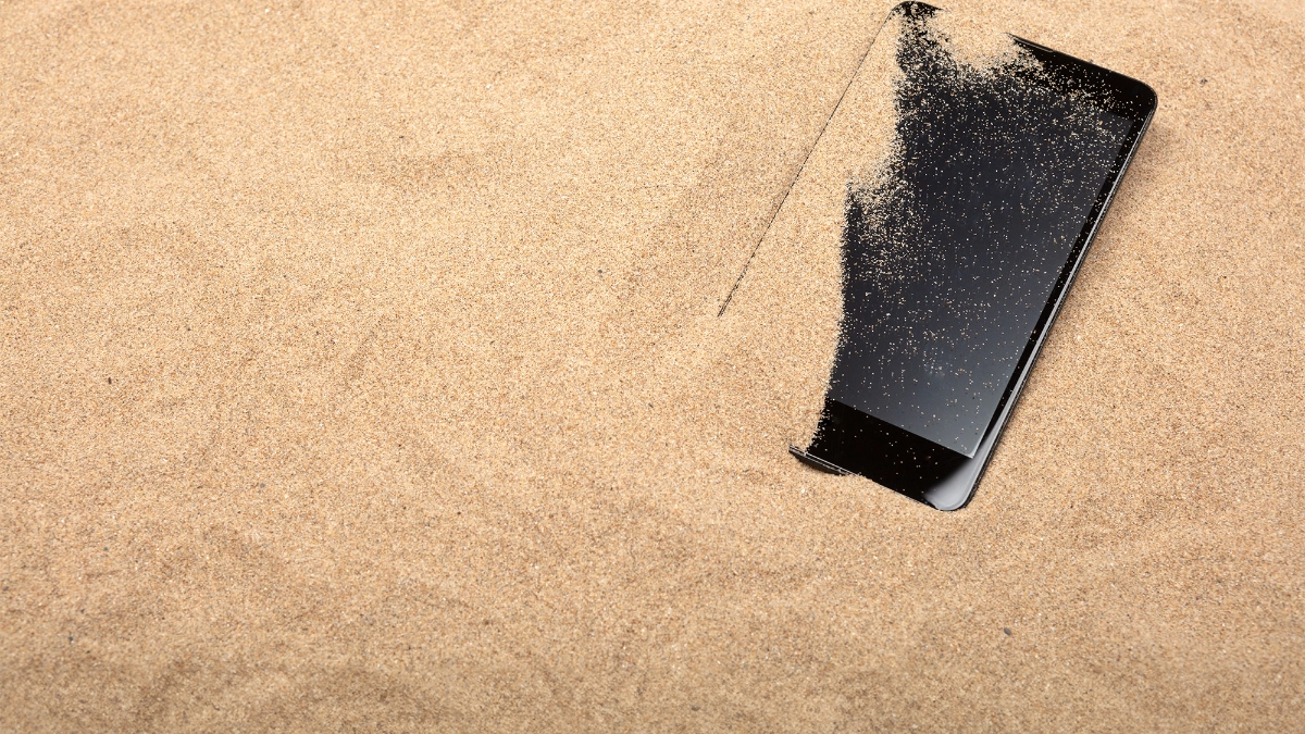 A photo of a mobile phone partially covered in sand on a beach